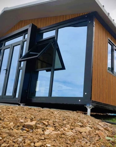 Modern prefabricated tiny home with wood paneling and large glass windows on a rocky hill.