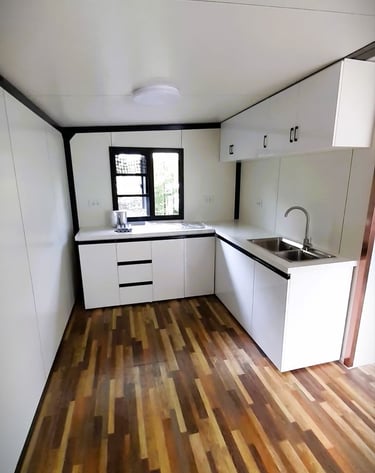 Modern tiny house kitchen with white cabinets, wood flooring, and a stainless steel sink.
