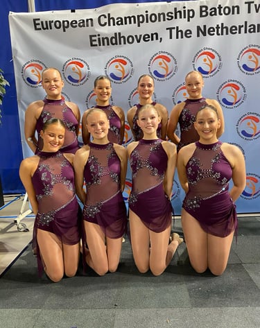 a group of young girls in purple dresses posing for a photo after a twirling competition