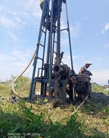 Construction workers using a manual rig for deep well drilling at a residential building site.