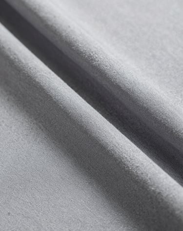 A close-up photograph of high-quality textile folds in shades of light gray and medium gray. The lighting is soft and diffused, capturing the delicate weave and sophisticated texture of the material in a clean, artistic composition.