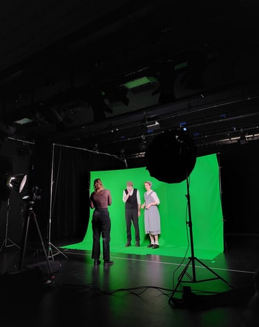 Zwei Schauspieler:innen in einem Greenscreen-Set, während die Regisseurin ihnen etwas erklärt.