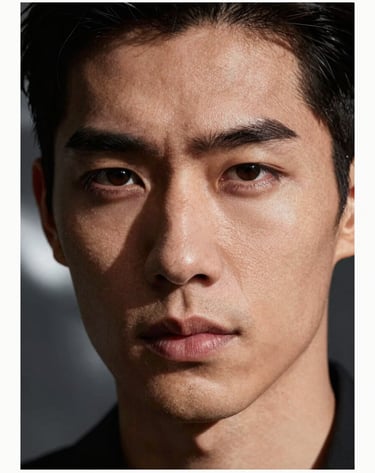 An extreme close-up portrait of a male model, high-impact lighting highlighting skin texture and sharp facial features. Background is a blur of deep charcoal and metallic silver tones.