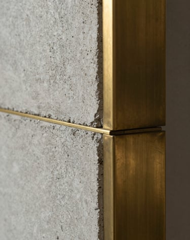 Close-up detail of a set construction, showing the intersection of raw concrete and polished brass, elegant and creative textures, Western European / French craftsmanship, cinematic lighting.
