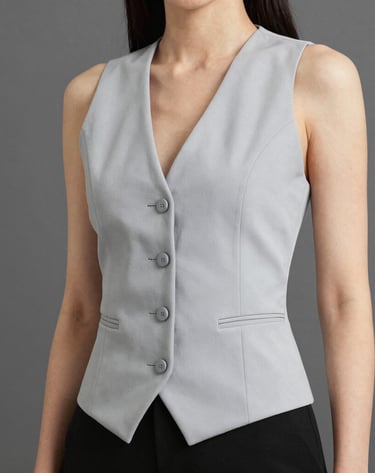 A woman wearing a tailored light grey button-up waistcoat vest with black trousers.