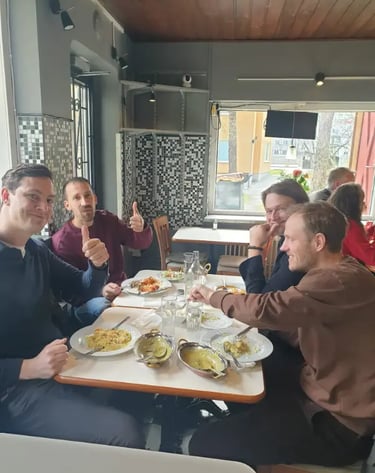 Four men enjoying a traditional Indian curry meal at a restaurant table with thumbs up.