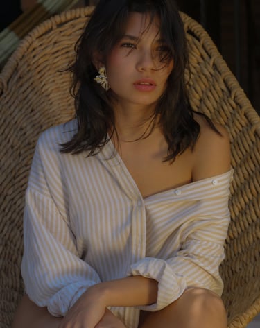 Joven mujer posando con una camisa medio hombro y pendientes dorados viendo el atardecer