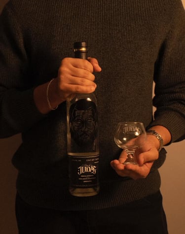 A person holding a bottle of Alma de Judas Mezcal and an empty tasting glass.