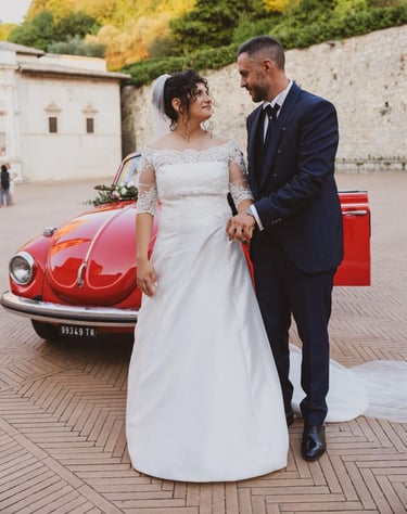 Sposi che si guardano innamorati in una suggestiva piazza con il maggiolone sullo sfondo.