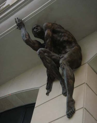 A bronze muscular male atlas sculpture crouched against a stone building corner as an architectural feature.