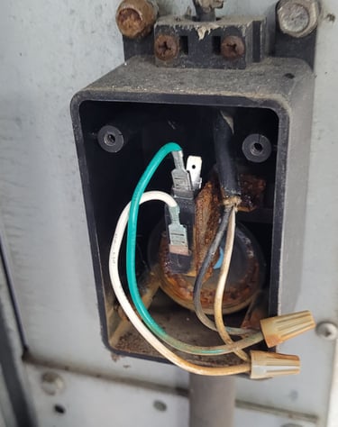 Exposed outdoor electrical junction box with rusted components, wire nuts, and colored wiring.