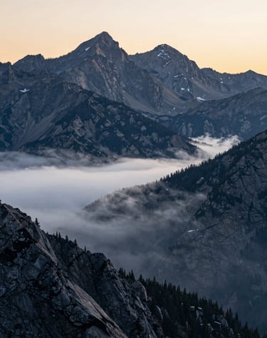 A majestic landscape of the North American / US Rocky Mountains at sunrise, captured with a telephoto lens, light silver mist and charcoal gray peaks.