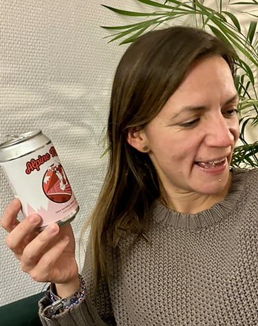 Une femme en pull gris tenant une canette de boisson énergisante naturelle Alpine Mate