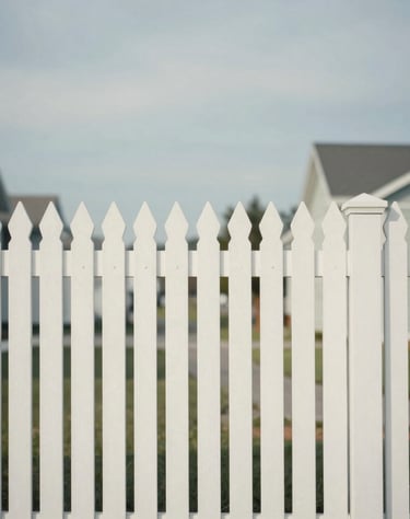 A minimalist view of a white picket fence in a North American suburb under a soft, overcast sky. The composition emphasizes geometric patterns and quiet elegance in off-white and soft blue-grey.