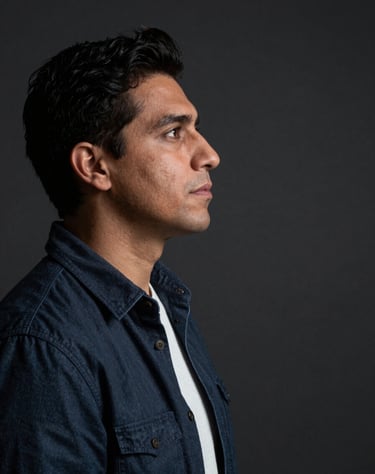 A portrait of an artist in profile, looking at a blank space, in a dark studio. Soft focus, dramatic lighting, contemporary Latinoamericano / Español attire.