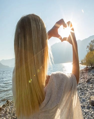 Orlane making a heart shape with her hands against a bright sunset over a mountain lake.