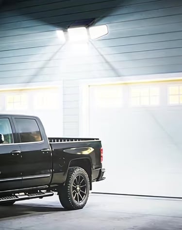 Solar powered motion sensor outdoor security light illuminating a driveway and black pickup truck at night.