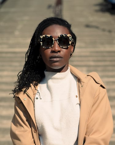 Portrait d’une modèle en manteau beige et lunettes léopard, posant sur des marches en plein soleil, regard confiant face à l’