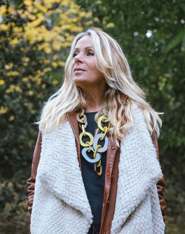 Portrait d’une modèle en extérieur, regardant sur le côté, portant un manteau clair et un collier imposant, avec un fond de f