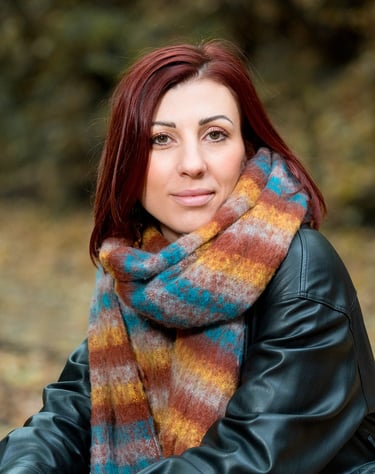 Portrait d’une comédienne en extérieur, vêtue d’une écharpe colorée et d’un blouson en cuir, avec un regard doux et confiant.