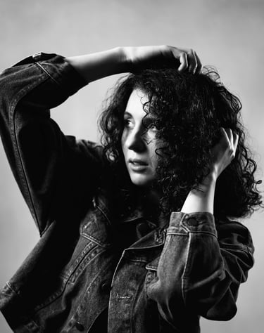 Portrait en noir et blanc d’une modèle aux cheveux bouclés, posant avec les bras levés dans une lumière contrastée.