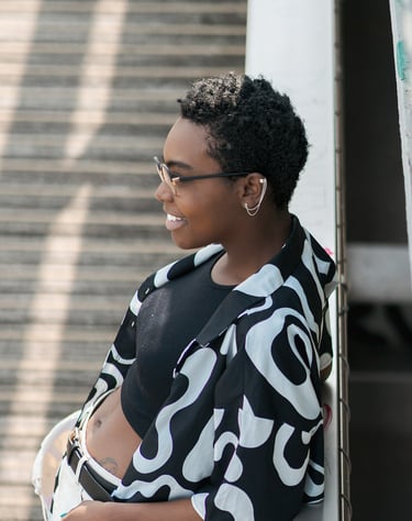 Portrait d’une modèle souriante en tenue noire et blanche, posant de profil contre une rambarde, avec un escalier en arrière-