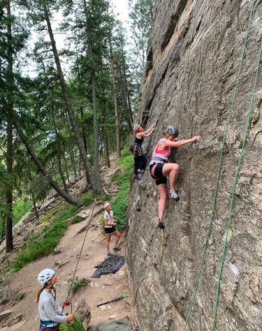 Two people climbing near each other outdoors, each with a belayer