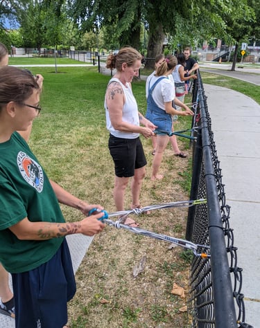A group of people typing climbing anchors on a park fence
