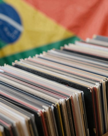 Vinyl records stacked in a collection, a glimpse of a South American flag in the blurred background, soft coral and charcoal colors.