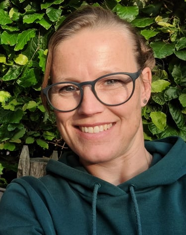 Marjolein Bisschop lachend portret in de natuur met groene bladeren als achtergrond