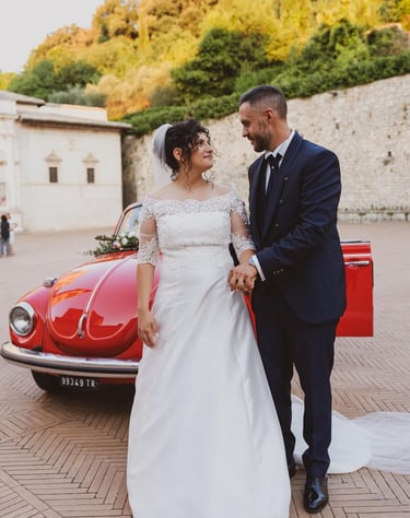 Sposi che si guardano innamorati in una suggestiva piazza con il maggiolone sullo sfondo.