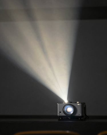 Cinematic photography of a projector beam in a dark theater, dust particles visible in the light, soft off-white light against dark slate grey environment.