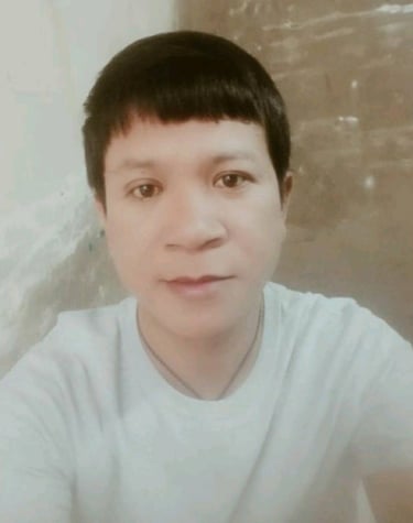 Man wearing a light shirt, looking at the camera indoors with a calm expression and soft lighting.