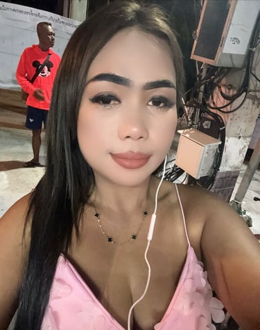 Lady wearing a pink top with headphones in left ear and a man standing in the background