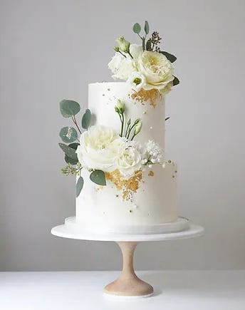 a white cake with white flowers and gold foil