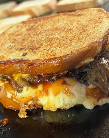 Grilled brisket and cheese sandwich from Slap Yo Self BBQ, featuring slow-smoked brisket, melted cheese, and BBQ sauce presse