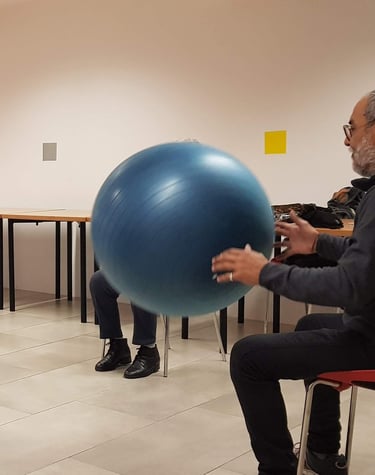Un grupo de personas mayores está sentado en círculo realizando ejercicios con una pelota como parte