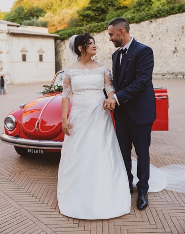 Sposi che si guardano innamorati in una suggestiva piazza con il maggiolone sullo sfondo.