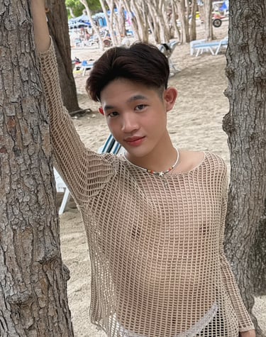 Young mad stood between 2 trees wearing a cream coloured mesh long sleeve top