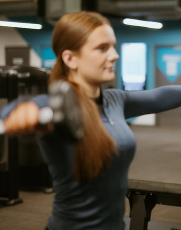 Client doing lateral dumbbell raise in Leamington Spa gym, coached by trainer focused on form and shoulder activation