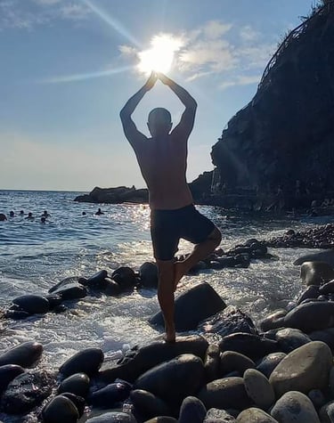 a man performing yoga on rocks in the sea