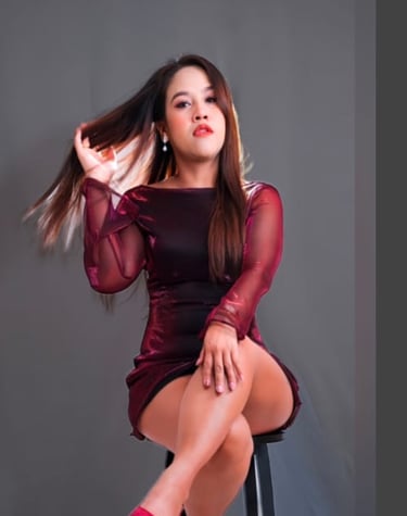 A lady sitting on a stool cross legged wearing a short long sleeve burgundy dress