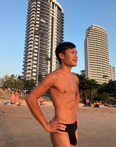 Man standing confidently on Pattaya Beach at sunset, with tall modern buildings and palm trees in the background.