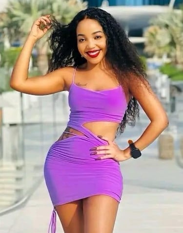 Woman standing with her arms raised, wearing a low crop short purple dress.