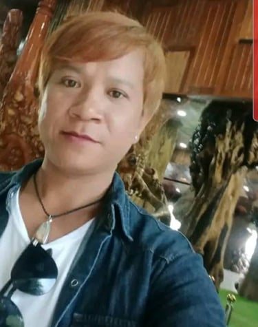 Man smiling indoors in Pattaya, Thailand, wearing a denim shirt and sunglasses on a white T-shirt.