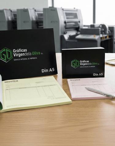 Custom printed invoice pads and business notebooks on a desk in a commercial printing shop.