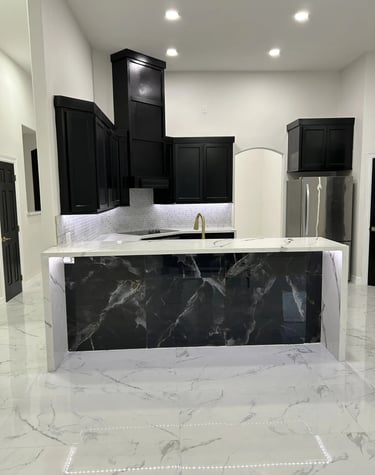 Modern luxury kitchen featuring a black marble island, white quartz countertops, and sleek black cabinets.