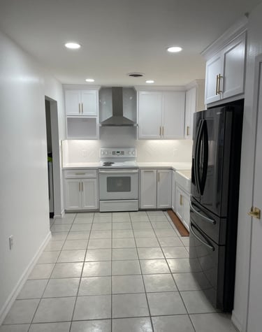 Modern white kitchen with gold hardware, stainless steel range hood, and black refrigerator.
