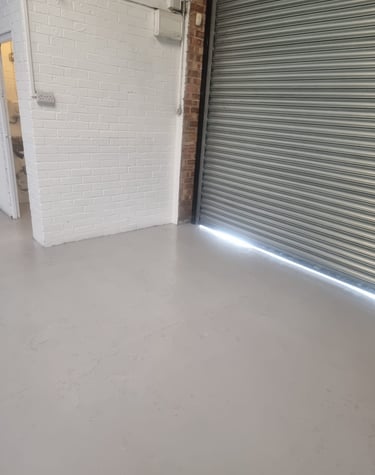 A close-up of a grey floor and a painted white brick wall, next to a garage shutter door.