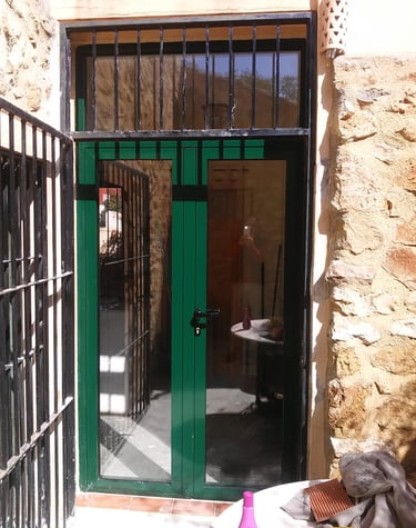 Puerta de aluminio color verde en casa rural de piedra.